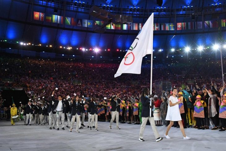 grupo de personas caminando en medio de estadio con bandera de juegos olímpicos 