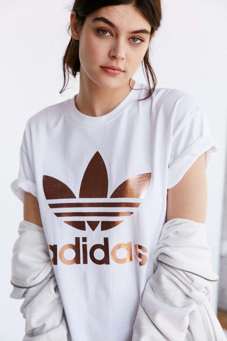 Mujer blanca con playera blanca y logo adidas rose gold