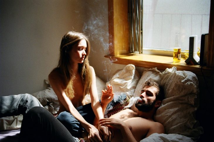 Pareja de novios recostados en una cama fumando un cigarrillo 