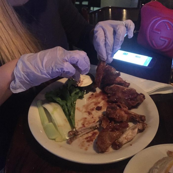 Chica comiendo alitas con guantes para no ensuciarse las uñas