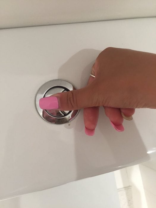 Chica tratando de oprimir un botón de inodoro con las uñas largas