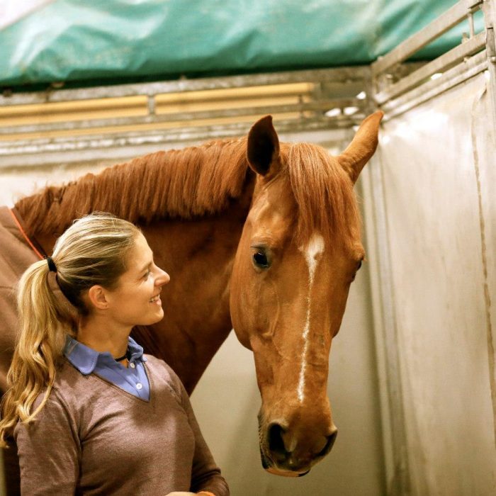 mujer rubia con sueter al lado de caballo cafe 