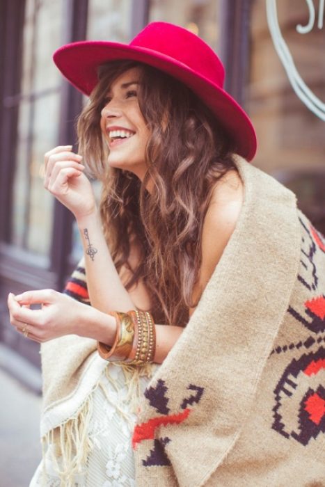 Chica usando un poncho y un sombrero rojo mientras está sentada en una banca riendo 