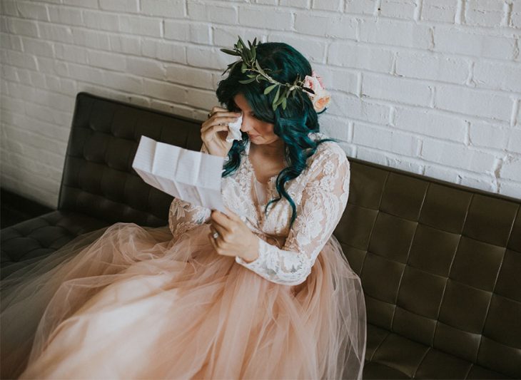 Chica sentada en un sofá leyendo una carta y llorando el día de su boda 