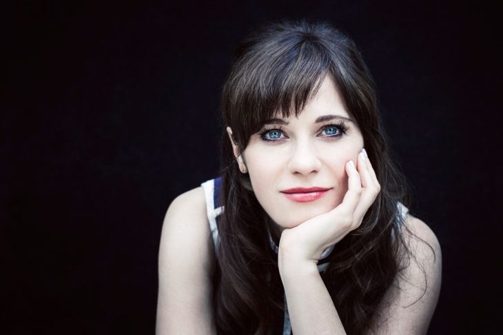 Zoey Deschanel con su mano sobre la barbilla sonriendo 