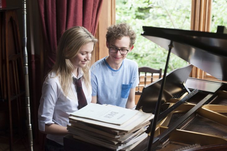 chica rubia con chico de lentes tocando el piano 