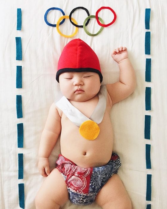 Bebé recostada en la cama disfrazada de ganador de medallas olímpicas 