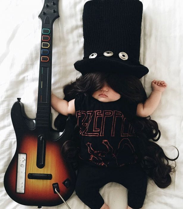 Bebé disfrazada de slash con una guitarra recostada en la cama 