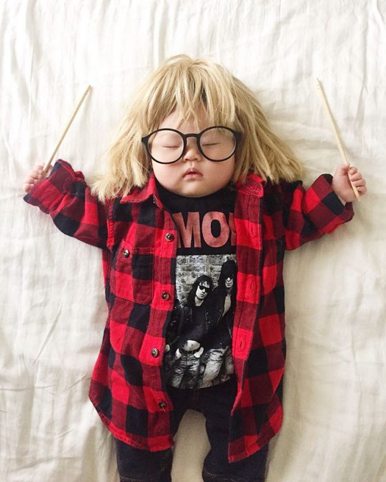 Bebé recostada en la cama disfrazada de Garth Algar del extraño mundo de Wayne 