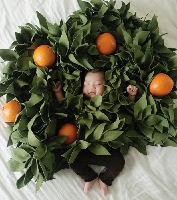 Bebé recostada en la cama disfrazada de árbol de naranjas 