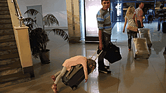Gif niña durmiendo en una maleta mientras su padre la lleva en el aeropuerto 