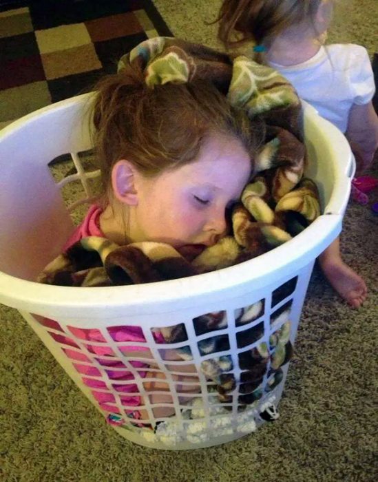 Niña durmiendo dentro de un cesto de ropa 