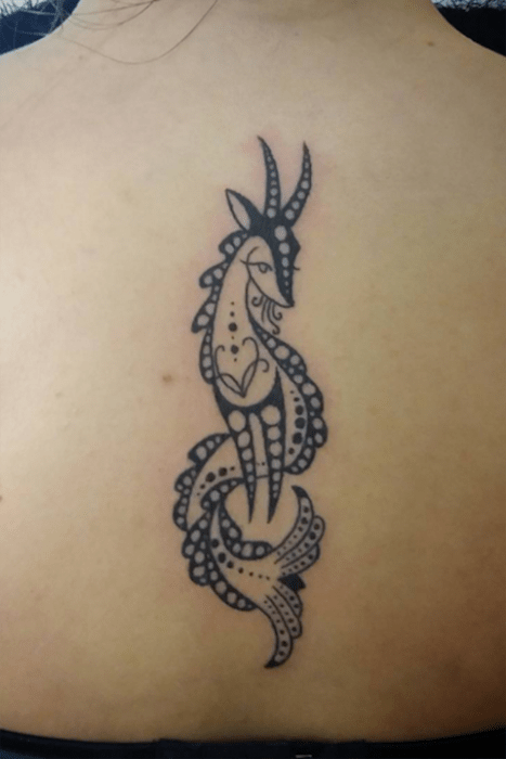 Chica con una cabra que representa el signo de capricornio tatuado en la espalda 