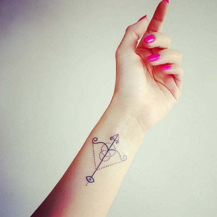 Chica con una flecha del signo sagitario tatuada en su mano 