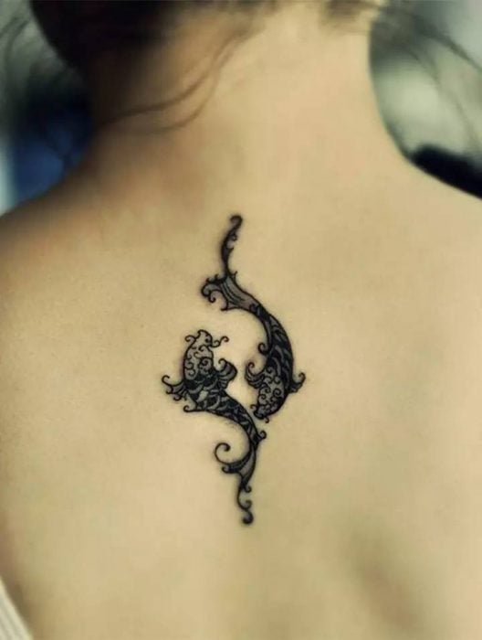 Chica con dos peces tatuados en la espalda 