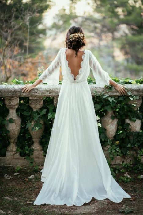 Chica con un vestido de novia con escote en la espalda parada sobre un barandal de piedra 