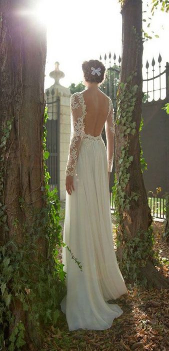 Chica con un vestido de novia con escote en la espalda entre dos árboles 