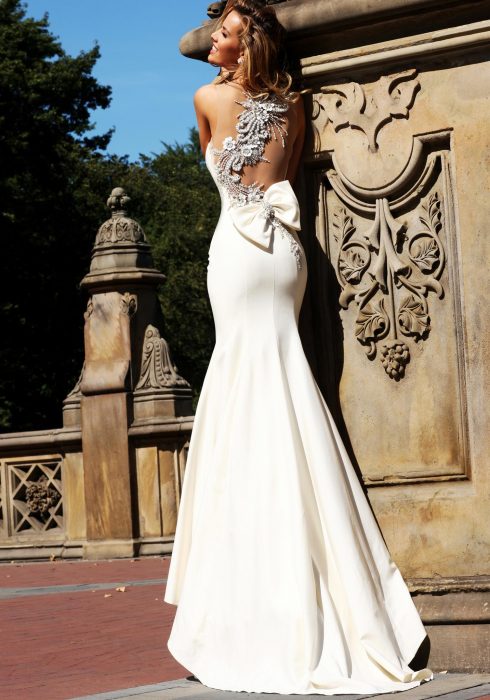 Chica con un vestido de novia con escote en la espalda parada sobre una columna de cantera 