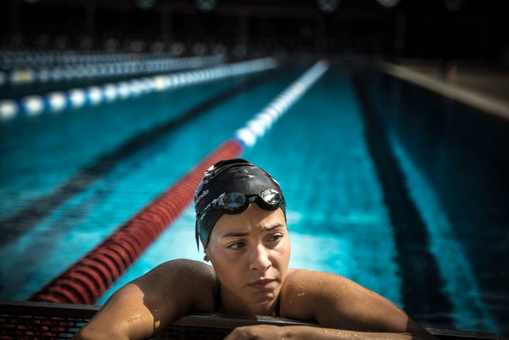 mujer con gorra y googles recargada en orilla de piscina