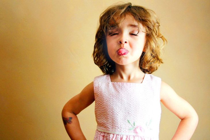 niña de cabello corto sacando la lengua con brazos en la cintura 