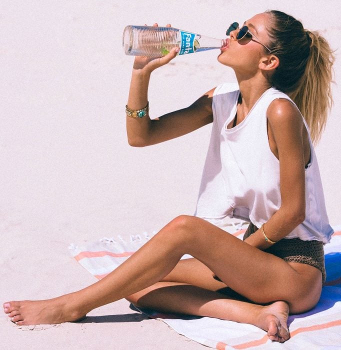 mujer rubia en la playa tomando agua de botella 