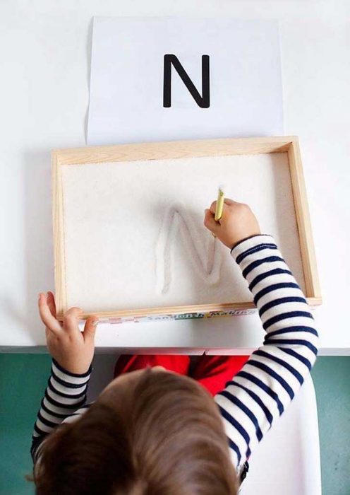 Niña escribiendo en una cajita con arena. 