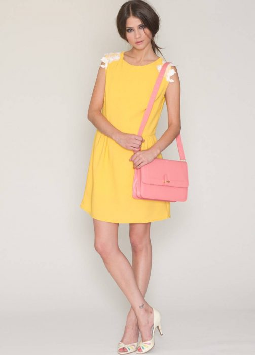 Mujer con vestido amarillo y bolsa rosa. 