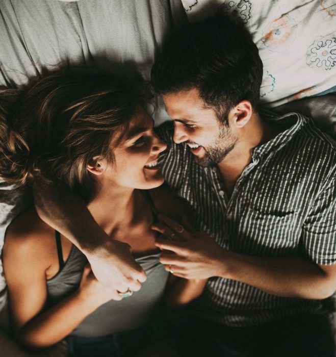 pareja sonriendo abrazada en la cama 