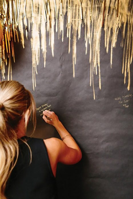 pared negra con rayada de dorado y mujer rubia escribiendo 