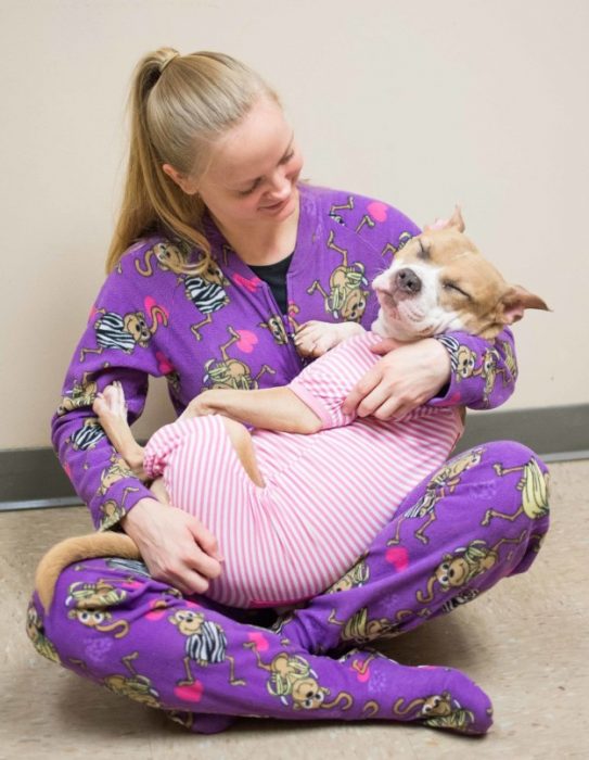 Chica cargando en brazos a un perro que está usando una pijama 