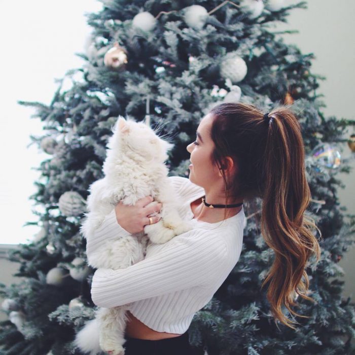 mujer de cabello largo abrazando a gato en arbol de navida 