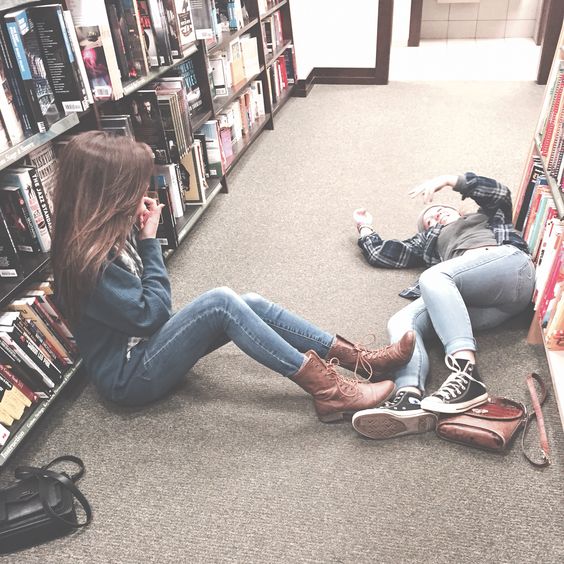 Chicas tiradas en medio de una biblioteca platicando. 