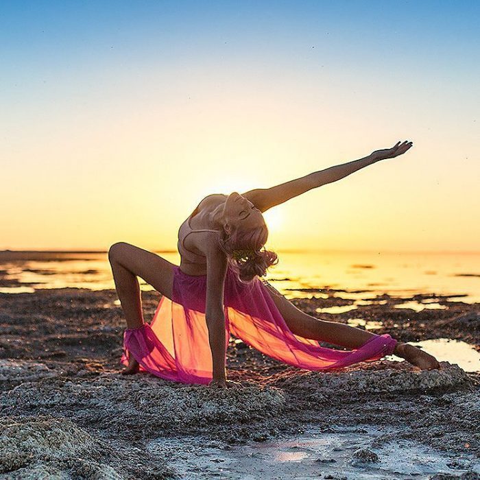 mujer se contorsiona en playa con atardecer 