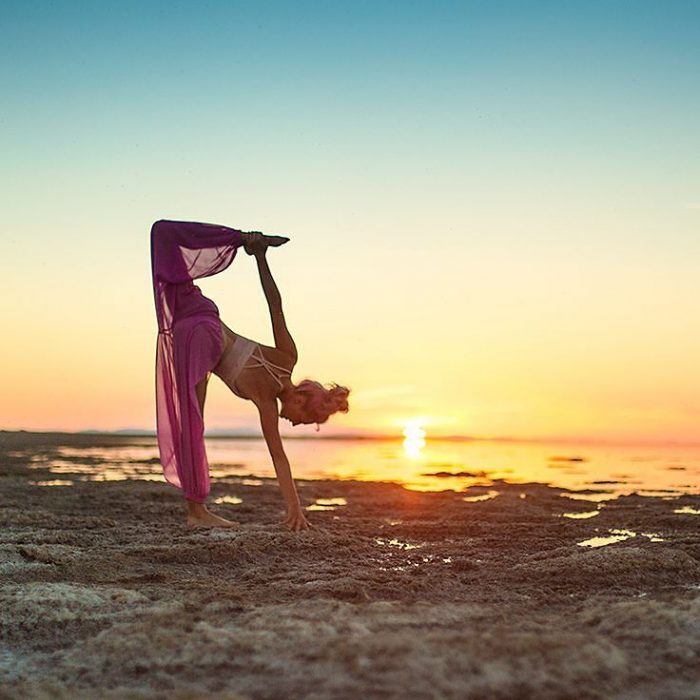 mujer se contorsiona en playa con atardecer 