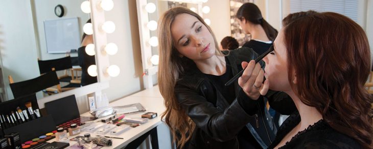 mujer de cabello largo maquillando a otra mujer