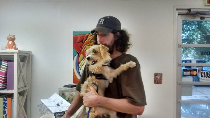 hombre de cabello largo con gorra cargando a perro 