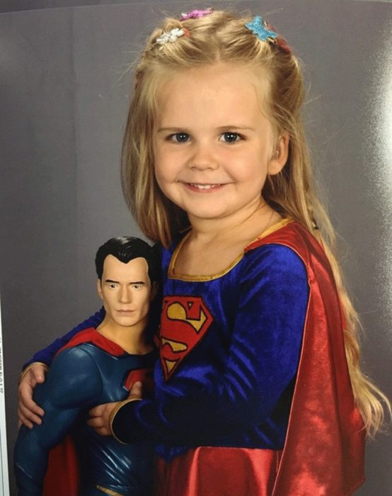 niña rubia con disfraz y juguete de superman 