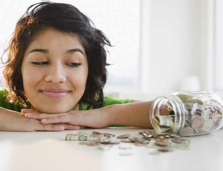 Muchacha viendo un frasco con monedas. 