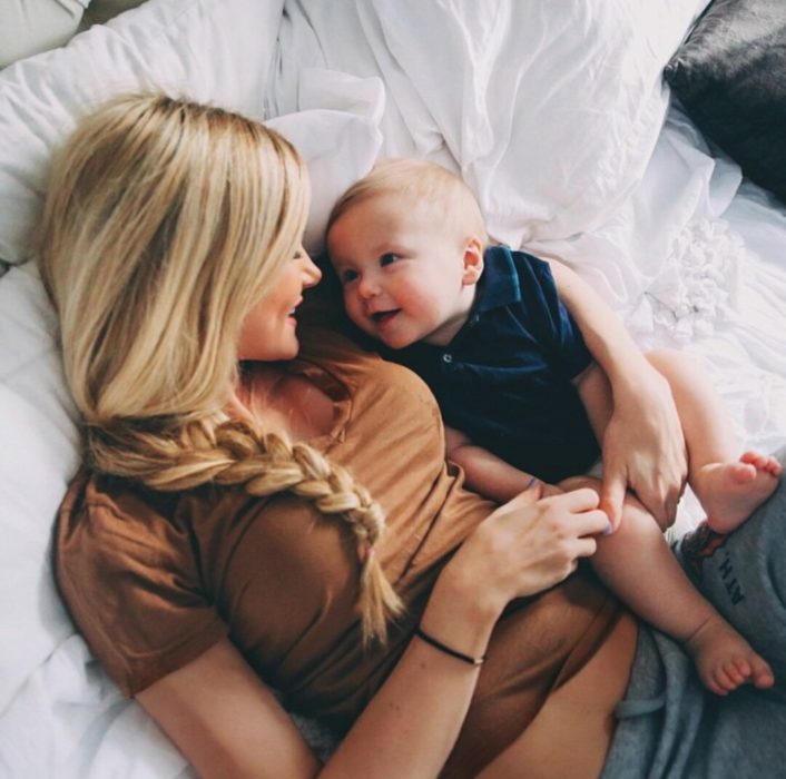 mujer rubia cargando a bebé en la cama 