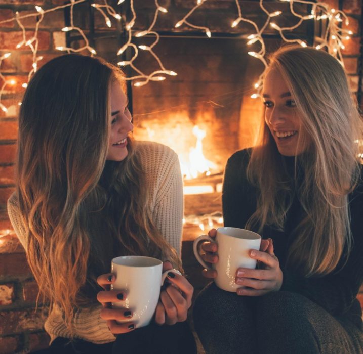 Mujeres rubias con tazas en chimenea con luces 