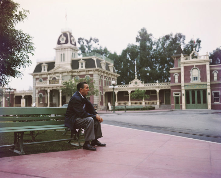 Walt disney sentado sobre una banca observando su parque de diversiones 