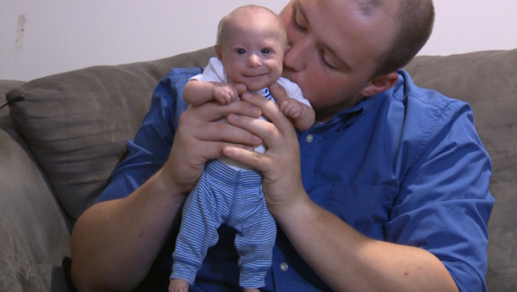 bebé que nació con enanismo siendo sostenido en brazos por su papá 