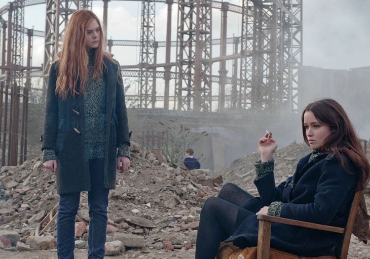 Chicas sentada entre los escombros, fumando mientras su amiga la observa 