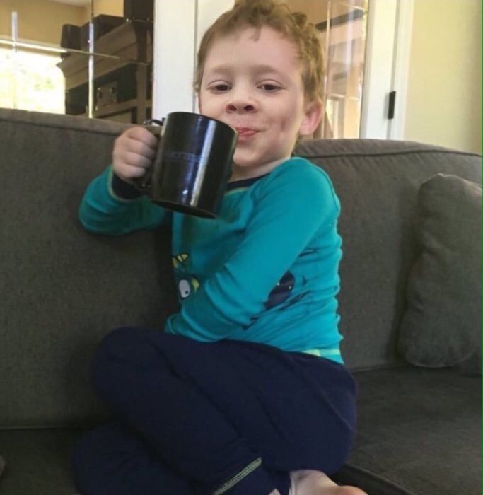 niño rubio con taza sentado y sonriendo