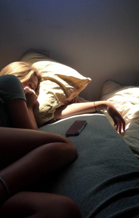 Chica recostada en la cama con el celular a un lado de su cama 