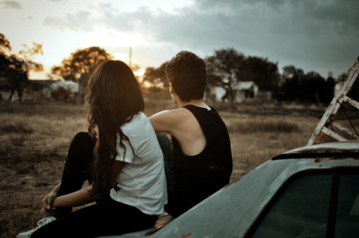 Pareja sentada en un coche viendo al horizonte 