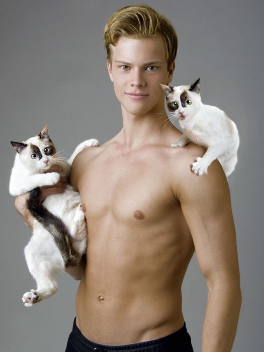 Modelo posando con dos gatos blancos con manchas. 