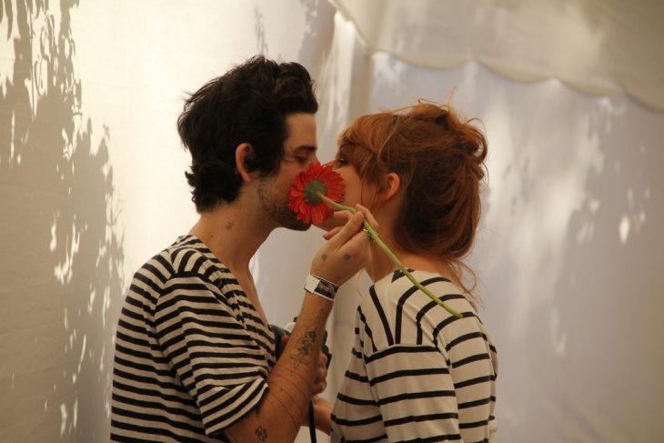 Pareja besándose detrás de una flor. 