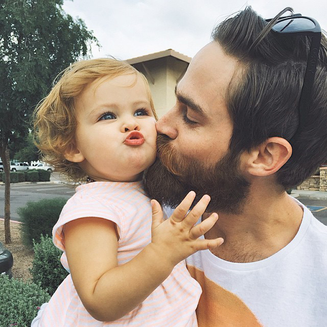 Papá con barba besando a su hija. 