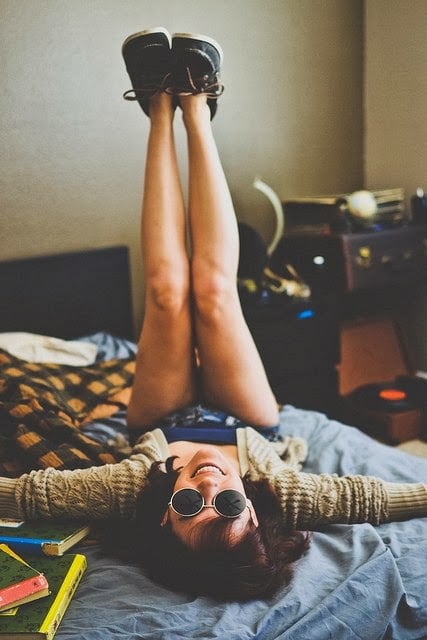 Chica sentada en la cama con los pies hacia arriba 